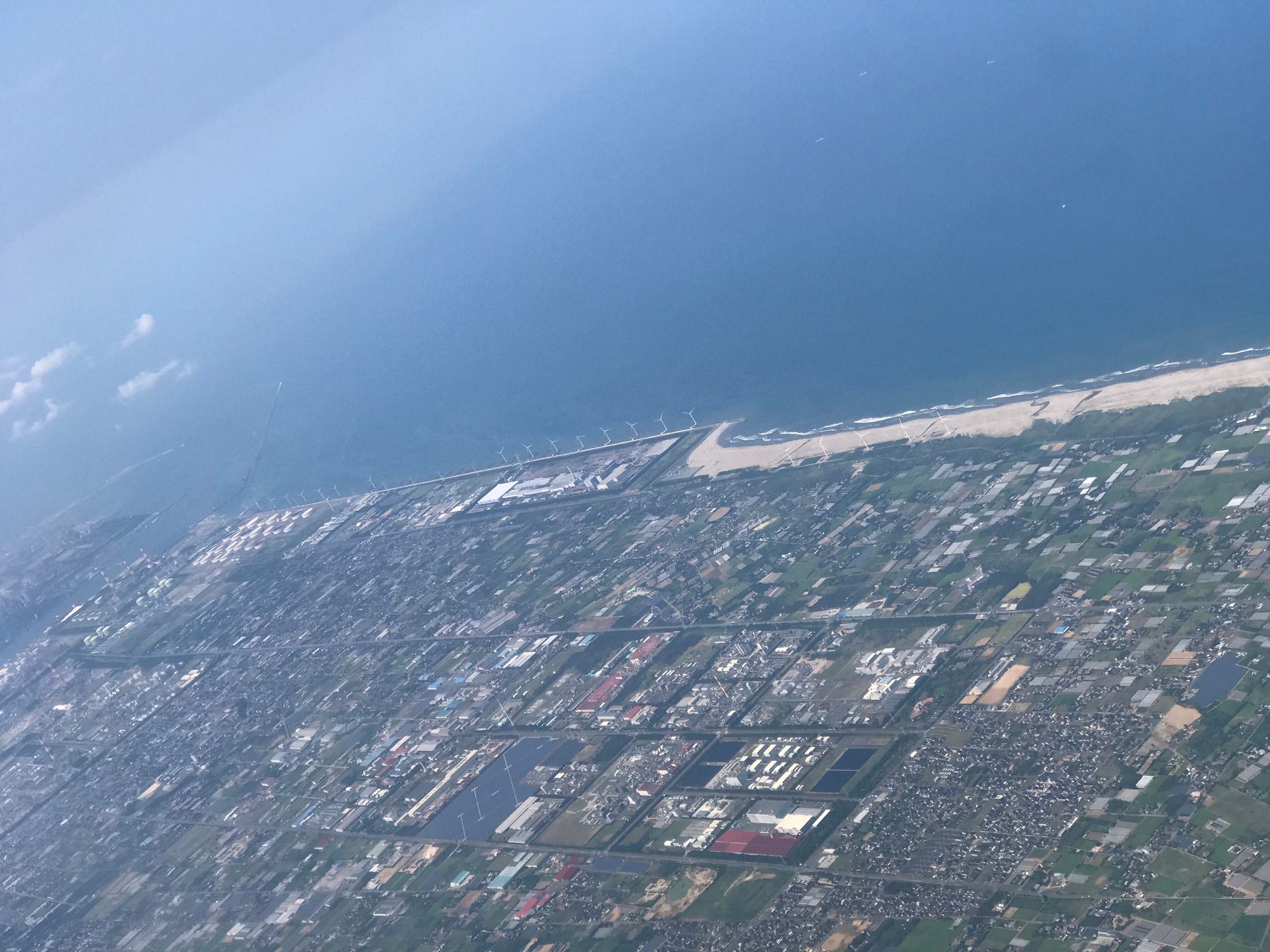 An aerial photo of a shoreline dotted with large wind turbines stretching along for at least a couple of kilometres