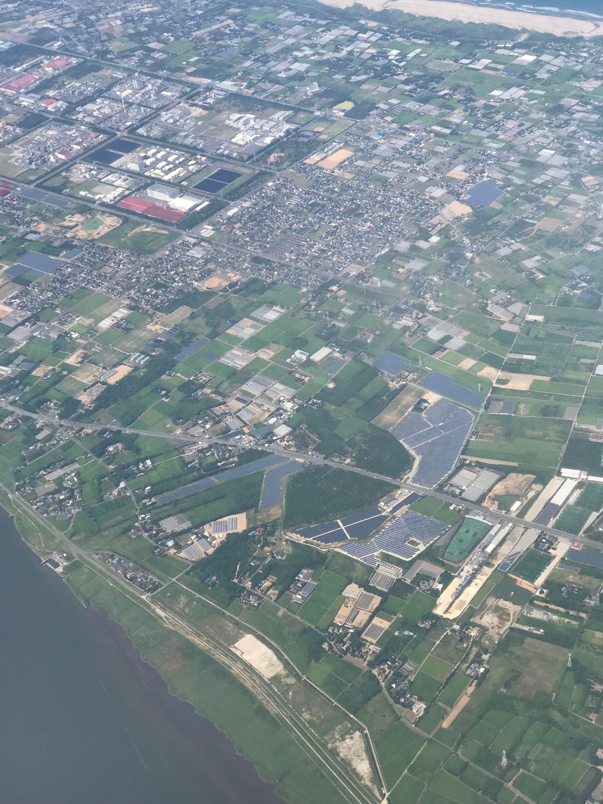 An aerial view of a part of the countryside around Tokyo with several large solar arrays in the middle of farmlands and houses