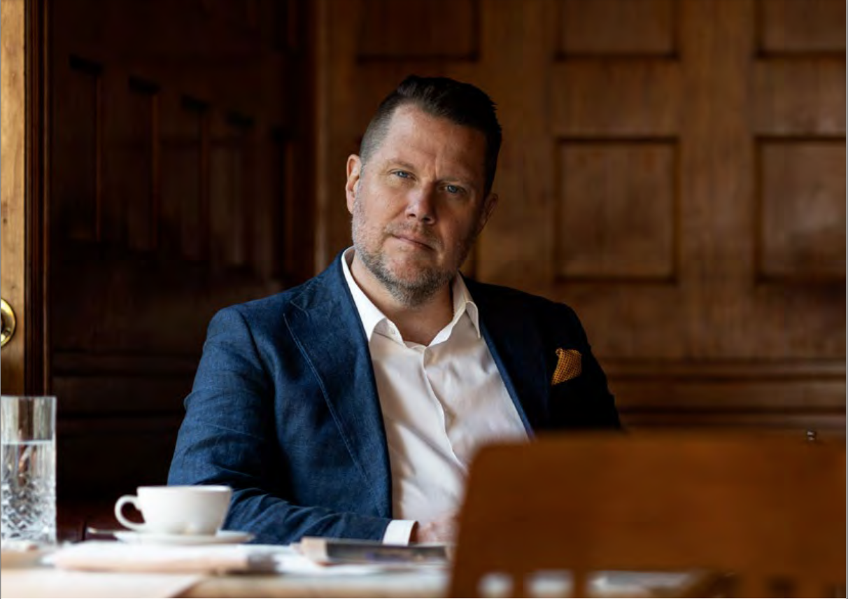 The CEO of Embracer group, seated at a table, wearing a suit, his head tilted to one side quizzically.