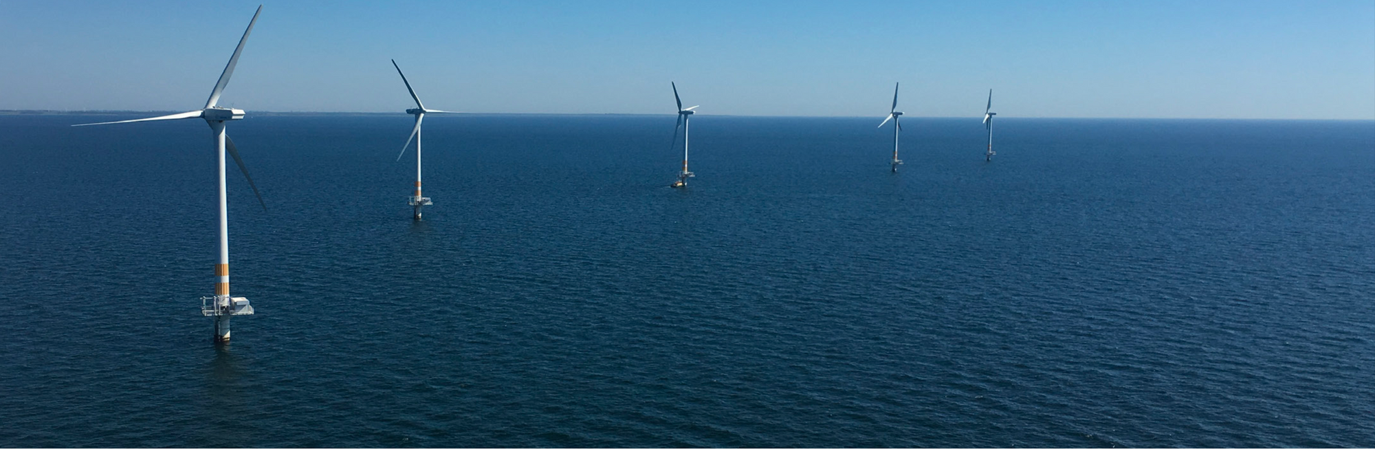 Five wind turbines stick out from the ocean.