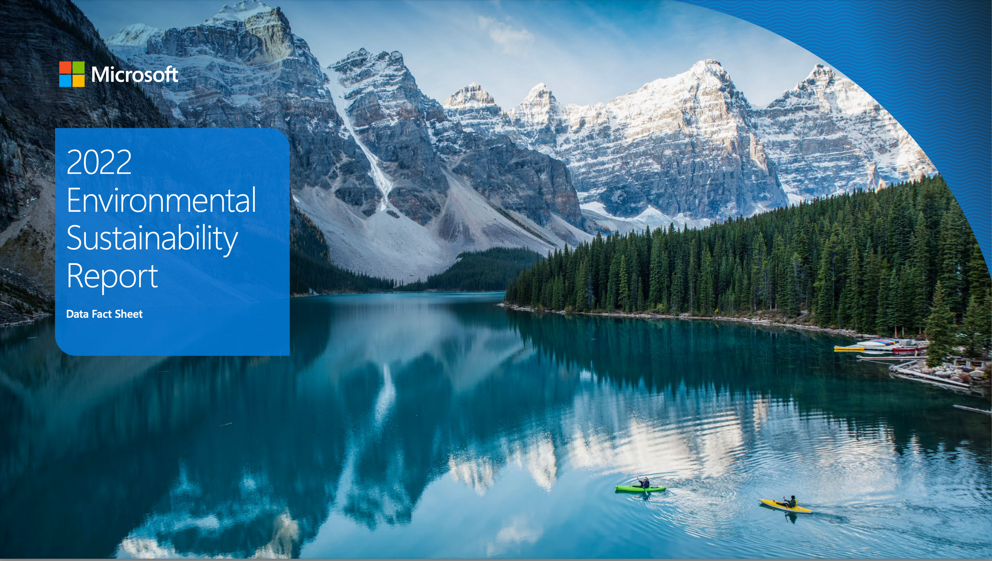 A blue glacier lake with two kayakers on it, tall mountains in the distance, and green forest on the shore.