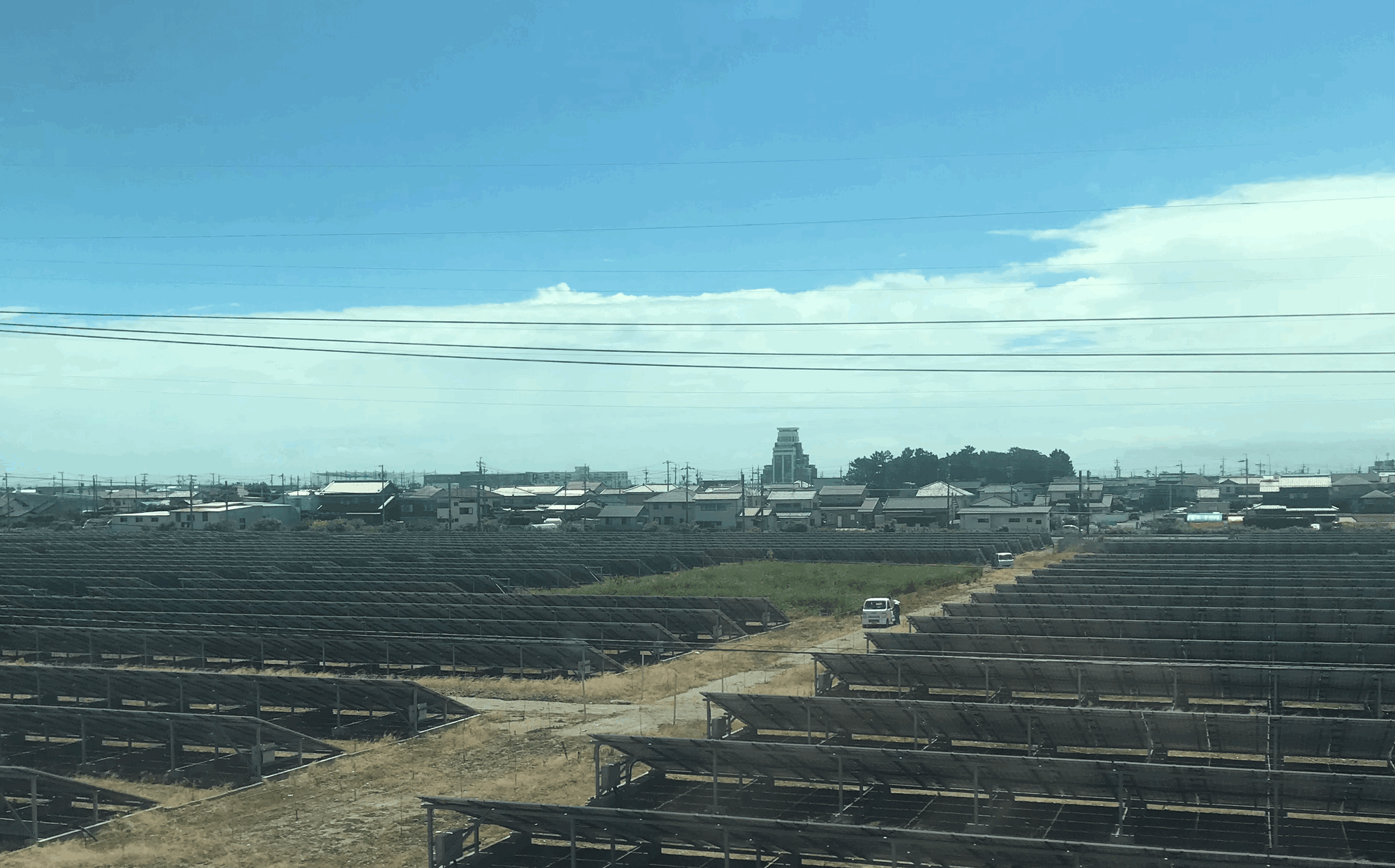 A solar array about the size of a football field, with panels tilted away from the camera, on a sunny day on the way to Kyoto