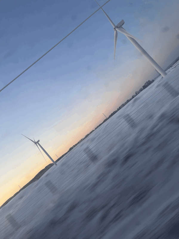 A photo taken from a train of a wind farm at dusk, with snow dusting the ground