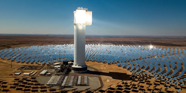 A tall tower stands in the middle of a desert, brightly lit with light shining from mirrors that surround it 